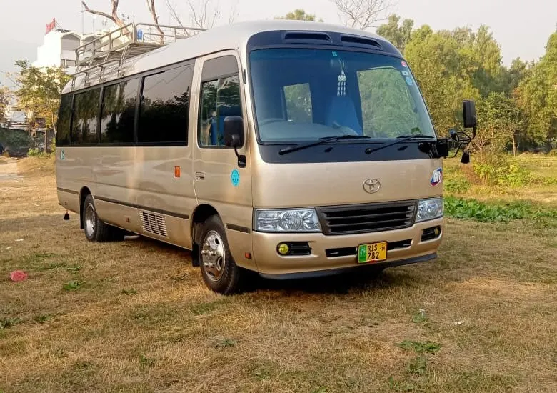 A champagne-coloured Toyota Coaster parked on grass beside a riverbank