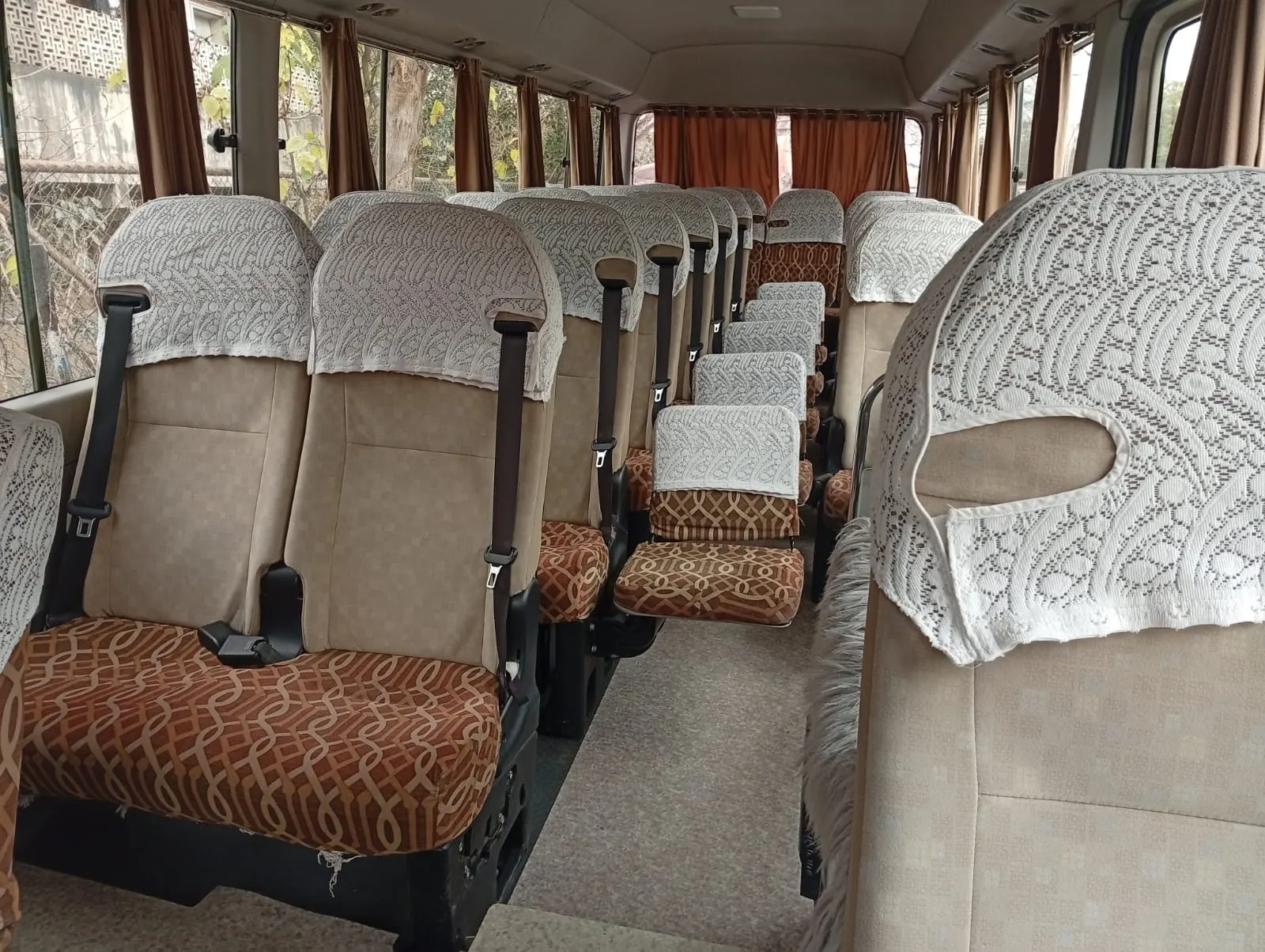 Inside a Toyota Coaster with cushioned seats and window curtains