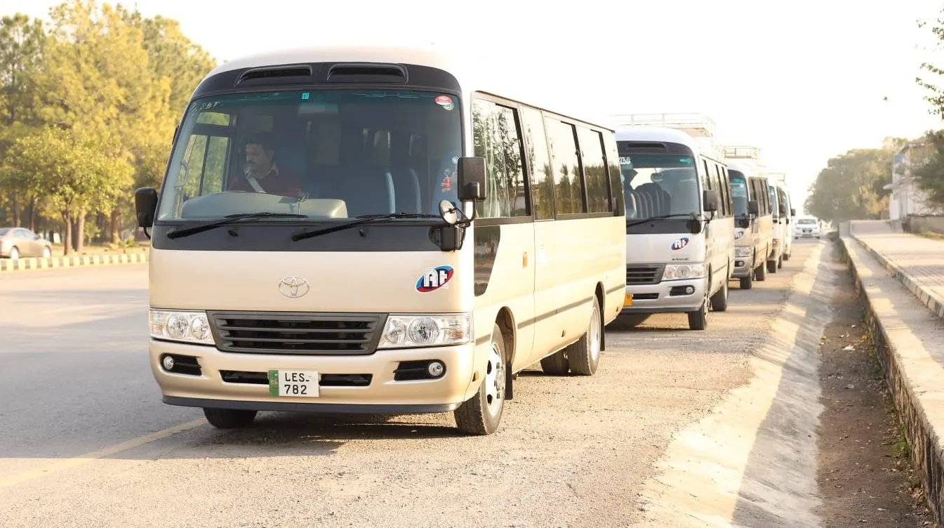 A Toyota Coaster with its driver at the wheel on an Islamabad road, more Amber Tours coaches waiting behind it