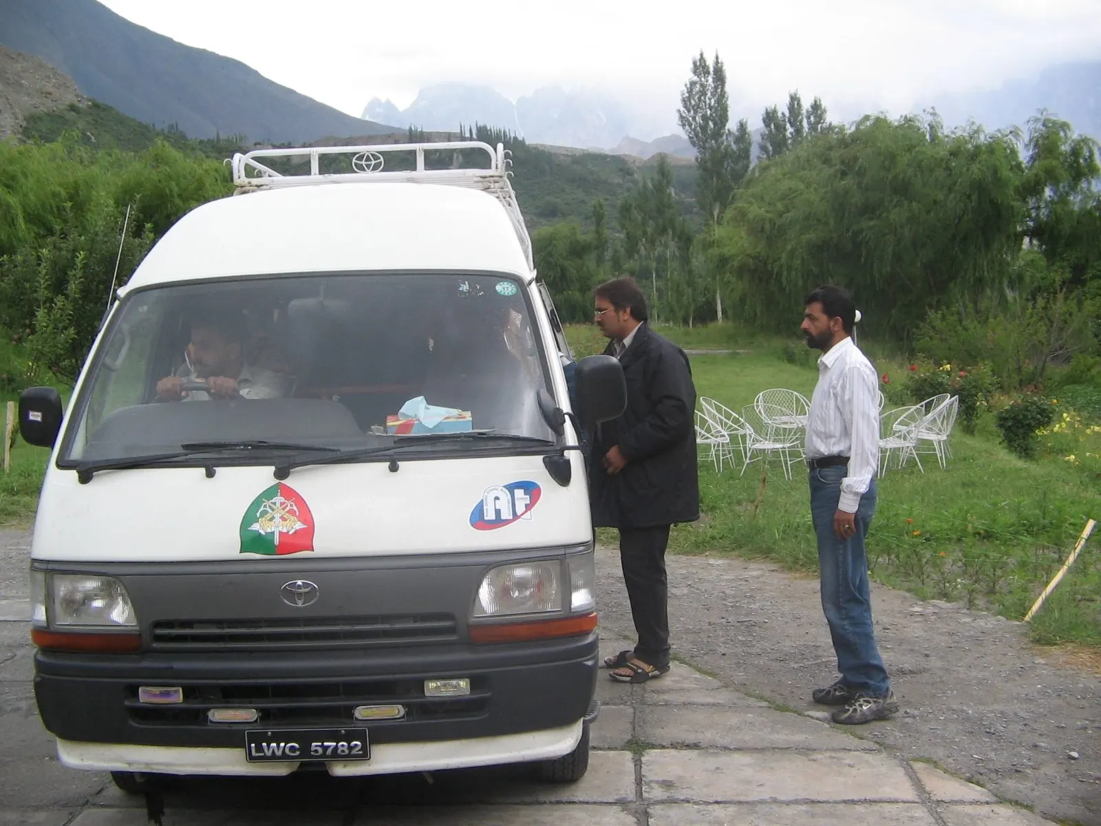 A Hiace van in the Hunza valley with two men talking beside it and mountains in the background
