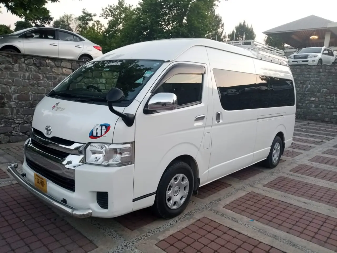 A white high-roof Toyota Hiace van parked on a paved forecourt